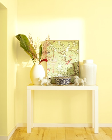 A white table with a collection of white vases, trinkets and abstract art sits against a Pineapple Grove-painted wall.