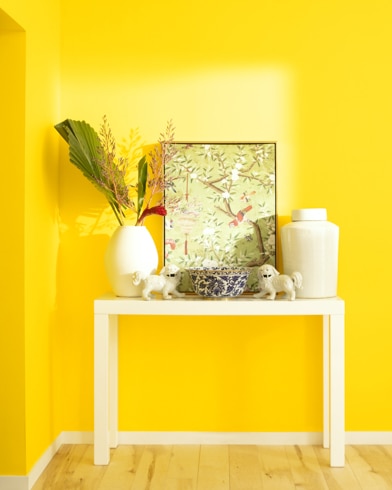 A white table with a collection of white vases, trinkets and abstract art sits against a Yellow-painted wall.