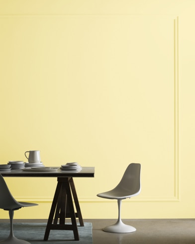 A midcentury modern dining table with two chairs sits in front of a wall painted Calla Lilly.