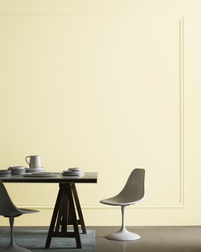 A midcentury modern dining table with two chairs sits in front of a wall painted Citron�e.
