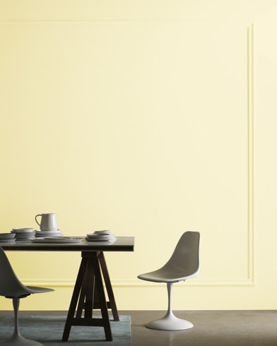A midcentury modern dining table with two chairs sits in front of a wall painted Counting Stars.
