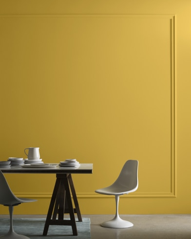 A midcentury modern dining table with two chairs sits in front of a wall painted French Quarter Gold.