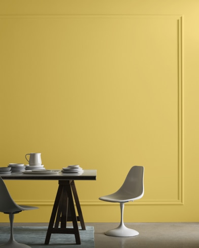 Una mesa de comedor moderna de mediados de siglo con dos sillas se ubica frente a una pared pintada de color dorado lujoso.
