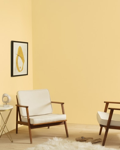 Una sala de estar pintada de color Topacio Amarillo, con dos sillas, una lámpara moderna y una alfombra peluda.