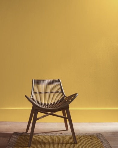 A modern rattan chair with a curved seat sits in front of a Antique Bronze-painted wall.