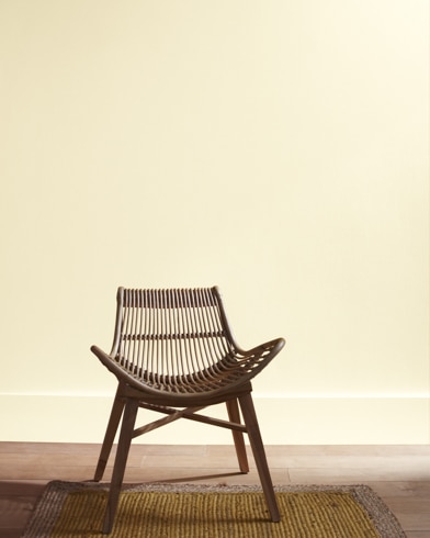 A modern rattan chair with a curved seat sits in front of a Fresh Air-painted wall.