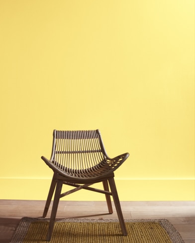 A modern rattan chair with a curved seat sits in front of a Good Morning Sunshine-painted wall.