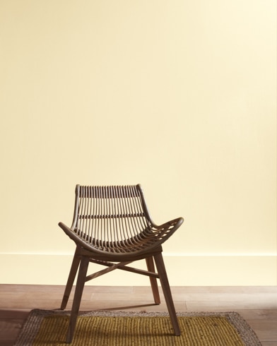 A modern rattan chair with a curved seat sits in front of a Happy Valley-painted wall.