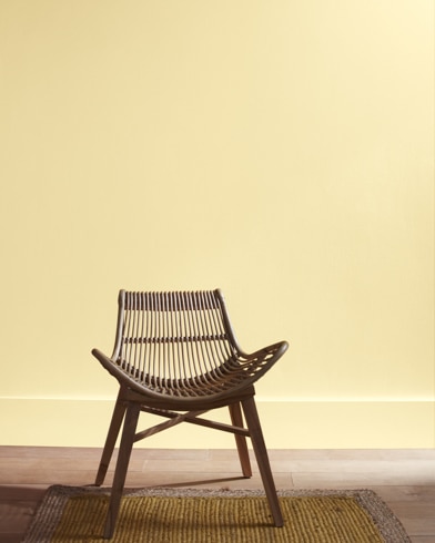 A modern rattan chair with a curved seat sits in front of a Harp Strings-painted wall.