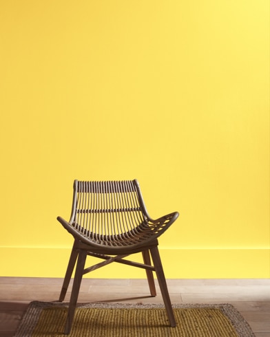 A modern rattan chair with a curved seat sits in front of a Sunbeam-painted wall.