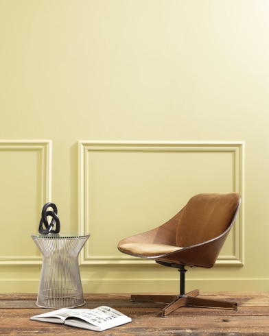 A flat wood riser holds a curved wooden chair, glass vase and open book in front of a paneled wall painted Beacon Hill Damask.