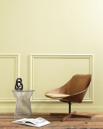 A flat wood riser holds a curved wooden chair, glass vase and open book in front of a paneled wall painted Stanhope Yellow.