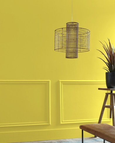A Bright Gold-painted living room hosts a wiry light fixture while a wood table and potted plant are just out of focus.