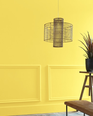A Cheerful-painted living room hosts a wiry light fixture while a wood table and potted plant are just out of focus.