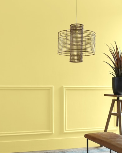A Mulholland Yellow-painted living room hosts a wiry light fixture while a wood table and potted plant are just out of focus.