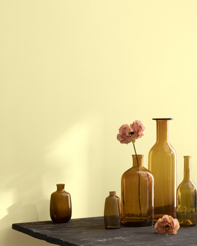 A collection of brown-tinted glass vases sit atop a wooden shop table next to a wall painted Fun in the Sun.