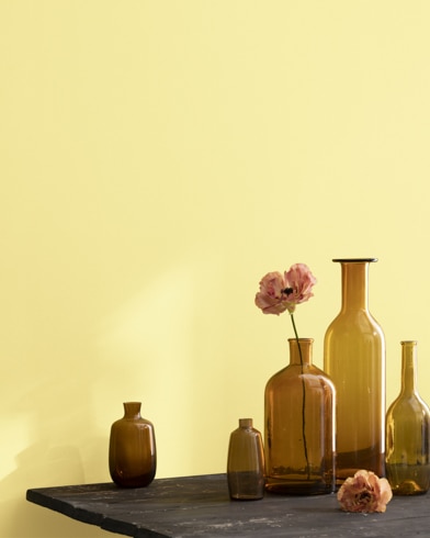 A collection of brown-tinted glass vases sit atop a wooden shop table next to a wall painted Jasper Yellow.