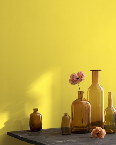 A collection of brown-tinted glass vases sit atop a wooden shop table next to a wall painted Lemon Grove.