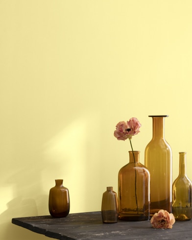 A collection of brown-tinted glass vases sit atop a wooden shop table next to a wall painted Lightning Storm.