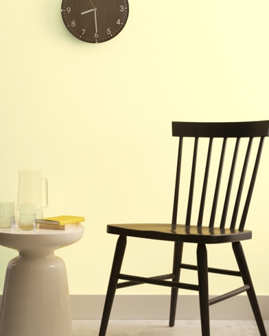 A brown clock hangs on a Butter-painted wall above a dark wood chair and small dining table.