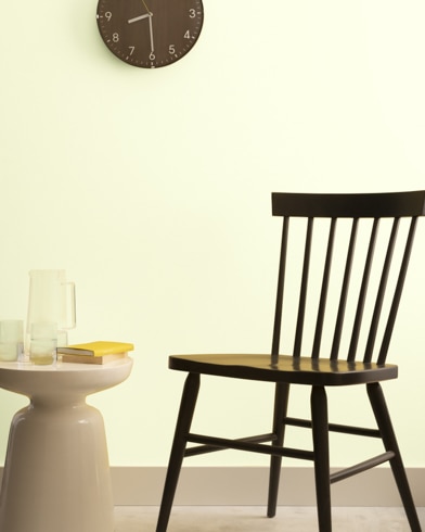 A brown clock hangs on a Eggshell-painted wall above a dark wood chair and small dining table.