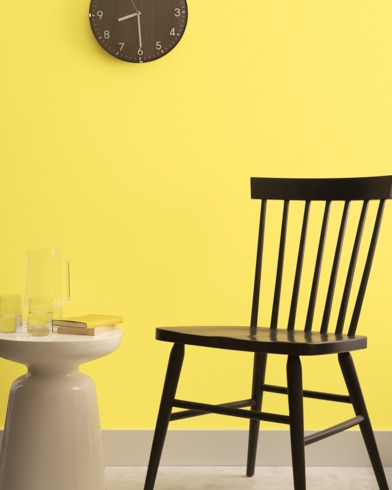 A brown clock hangs on a Sunburst-painted wall above a dark wood chair and small dining table.