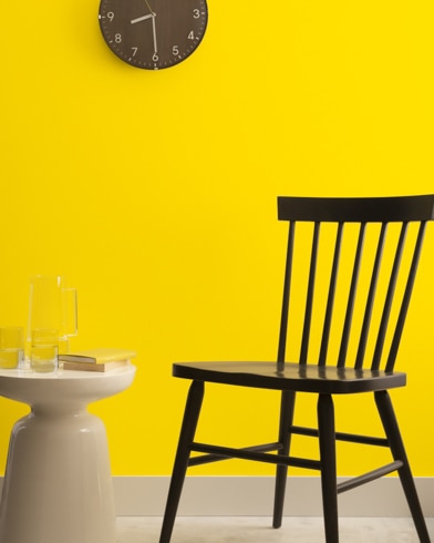 A brown clock hangs on a Sunporch-painted wall above a dark wood chair and small dining table.