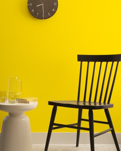 A brown clock hangs on a Yolk-painted wall above a dark wood chair and small dining table.