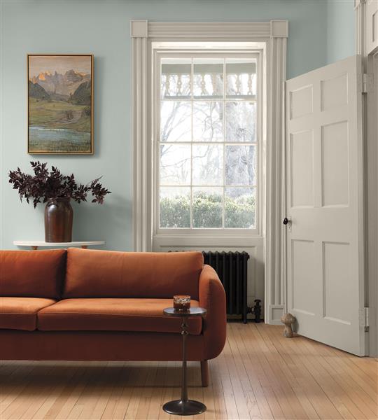 A living room with traditional architectural details and a burnt orange velvet sofa painted in White Down OC-131 and walls painted in Nelson Blue CW-635, part of the Colour Trends 2027 collection.