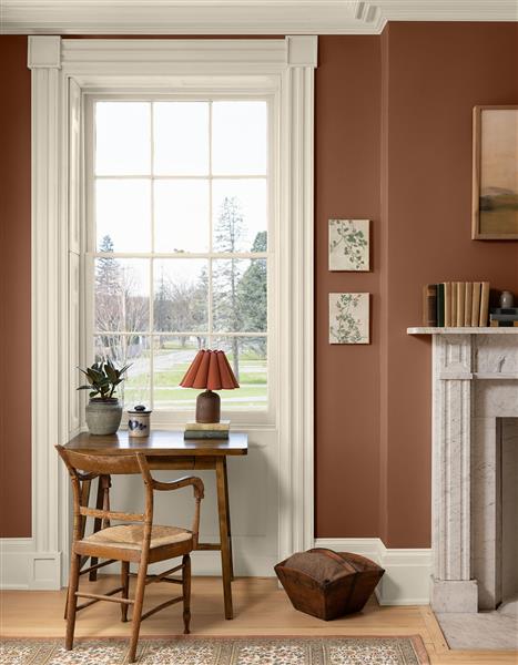 A living room space with a desk and chair next to a sash window. Walls are painted in Antique Copper 1169 and woodwork is painted in White Down OC-131.